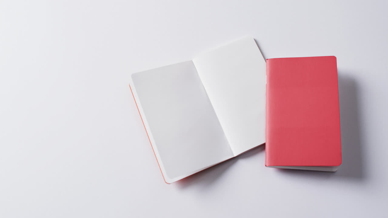 Close up of closed red book and open blank book with copy space on white background in slow motion