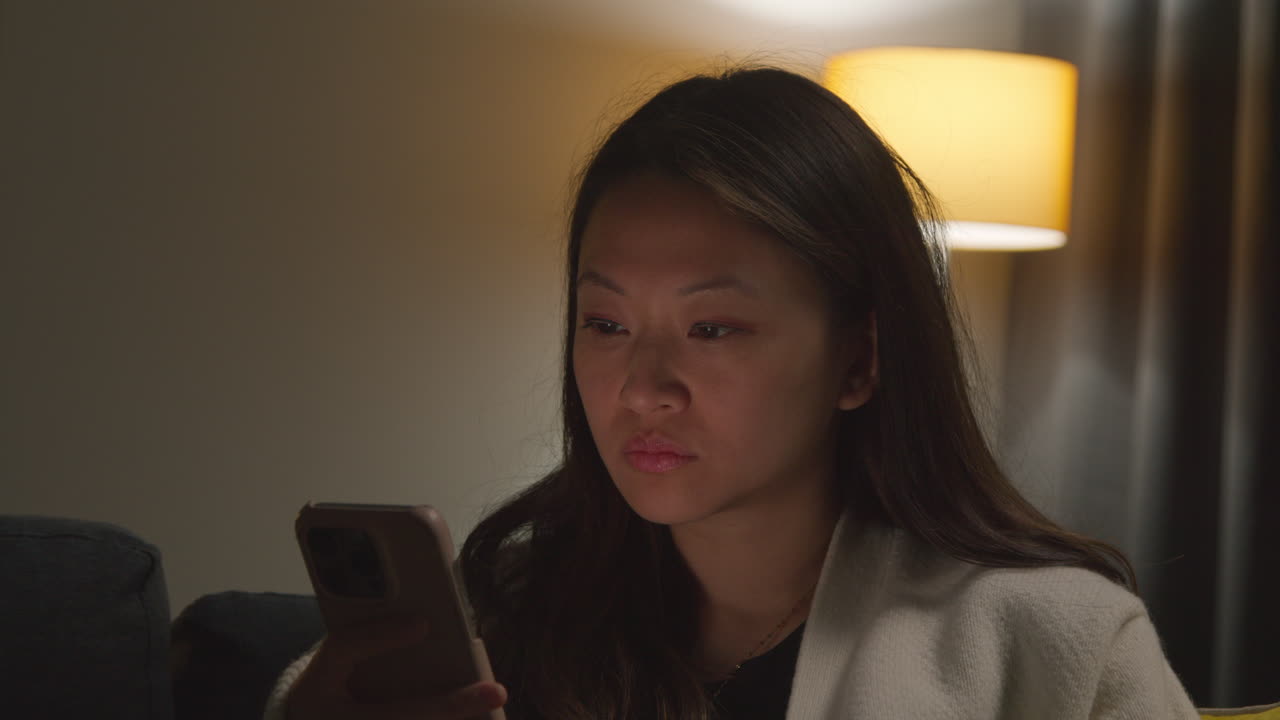 인터넷이나 소셜 미디어를 스크롤하는 휴대 전화로 소파에 앉아 집에서 저녁을 보내는 여성의 클로즈업