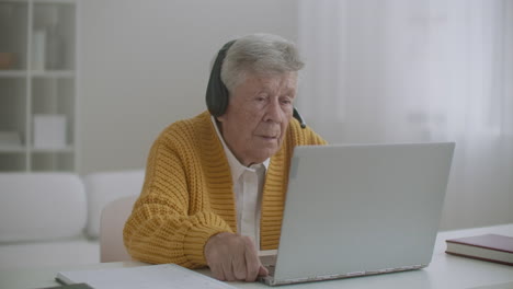 senior woman with laptop computer calling on smartphone at home. old woman having a video call on the laptop smiling and talking happily indoors in a cozy apartment. doctor video calling older patient