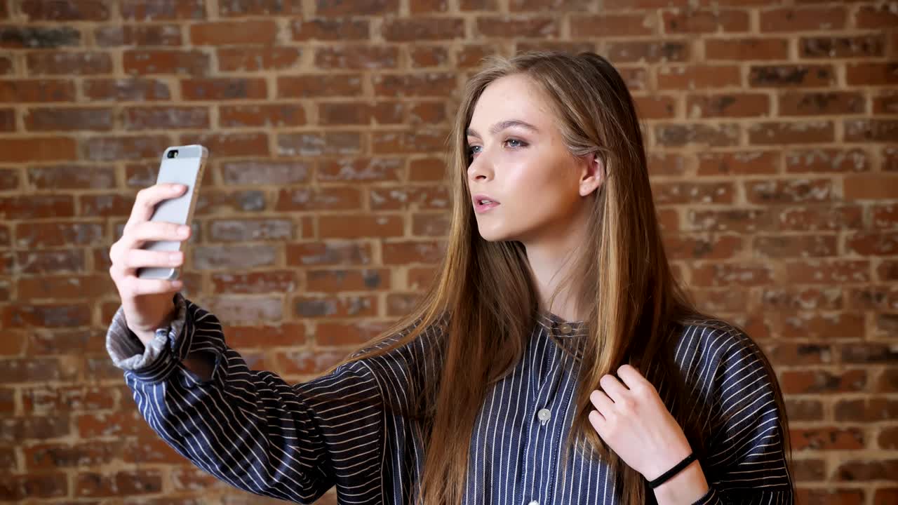 joven hermosa está haciendo selfie en su teléfono inteligente, concepto de comunicación, fondo de ladrillo