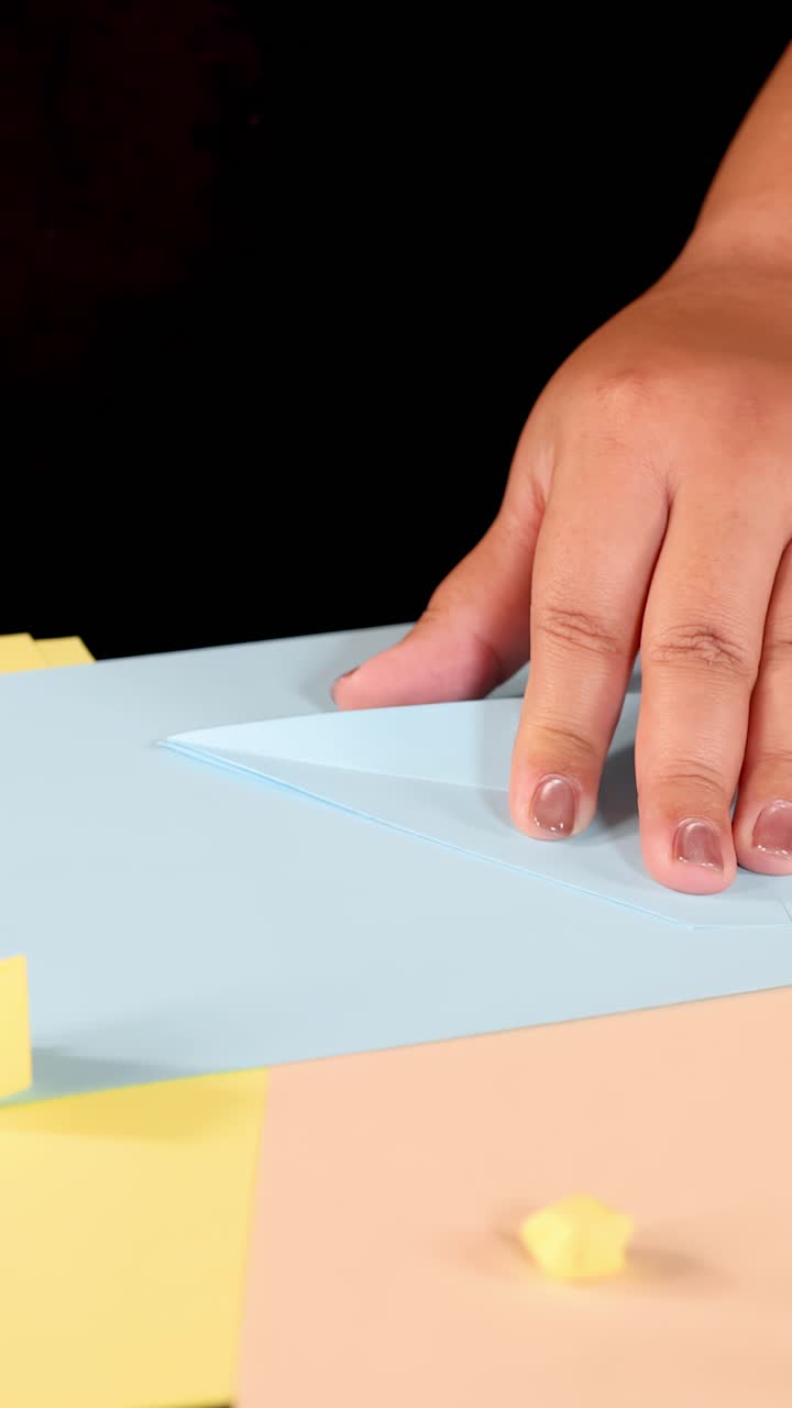 Una persona usa un taglierino per tagliare e piegare carta blu su una scrivania colorata e ben illuminata.