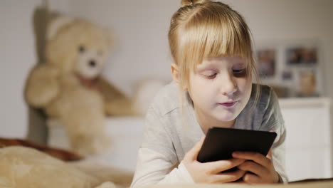 a 6-year-old girl reads an e-book in her bedroom lies on a bed
