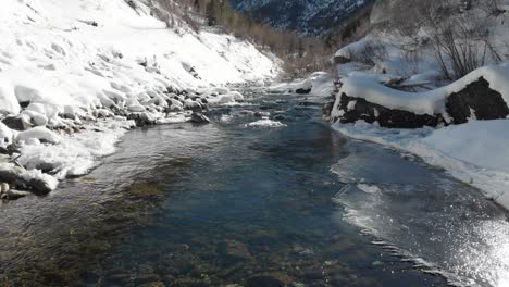 Low-aerial-flight-up-babbling,-snowy-white,-frozen-stream-in-winter