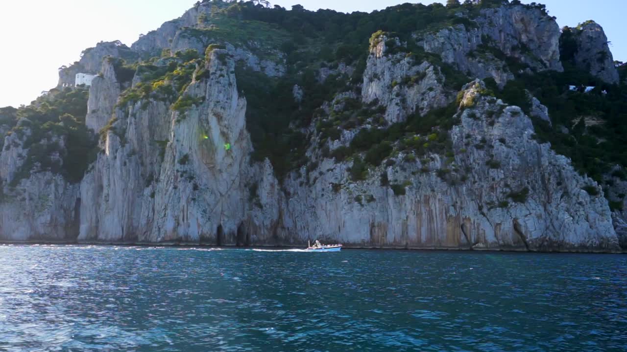 vista lateral de un barco a motor frente a un acantilado empinado de agua azul en capri, italia
