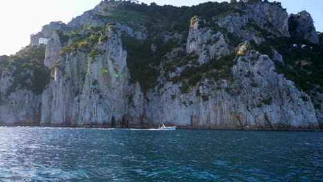 Vista-Lateral-Del-Bote-A-Motor-Frente-Al-Agua-Azul-Del-Acantilado-Escarpado-En-Capri,-Italia