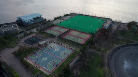 panoramic aerial clip of inner city sports complex, with tennis, basketball and baseball games under the floodlights