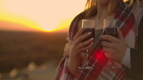 Man-and-young-pretty-woman-sitting-on-couch-holding-wine-glasses-and-kissing-on-rooftop-terrace-at-sunset