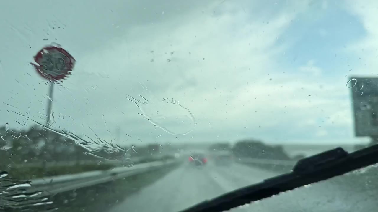 La pioggia battente cade sull'autostrada durante un viaggio nel pomeriggio mentre i tergicristalli lavorano per liberare la visuale per un viaggio sicuro.