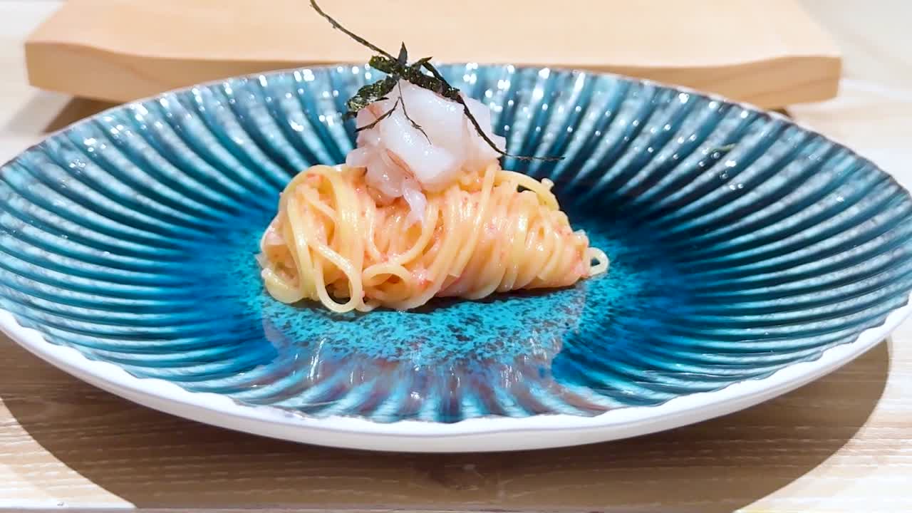 A beautifully arranged noodle dish garnished with seafood on a striking blue plate.