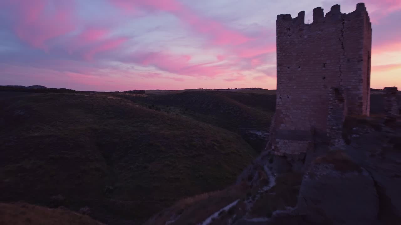 Drone shot of the medieval Oreja Castle perched on a hilltop at golden hour near Aranjuez, Spain. Scenic sunset over rural fields and rocky landscape.
