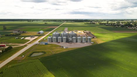 drone view of agro silos tower of storage of agricultural products and grain elevators in the middle of a green cultivated field, zooming in