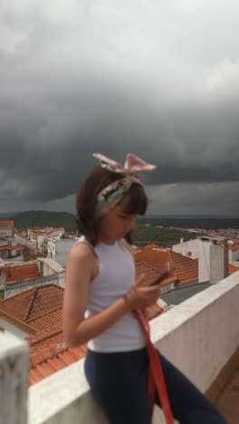 girl on rooftop with smartphone under dramatic clouds