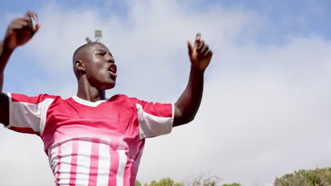 celebrating victory, african american male athlete raising arms, on field, copy space