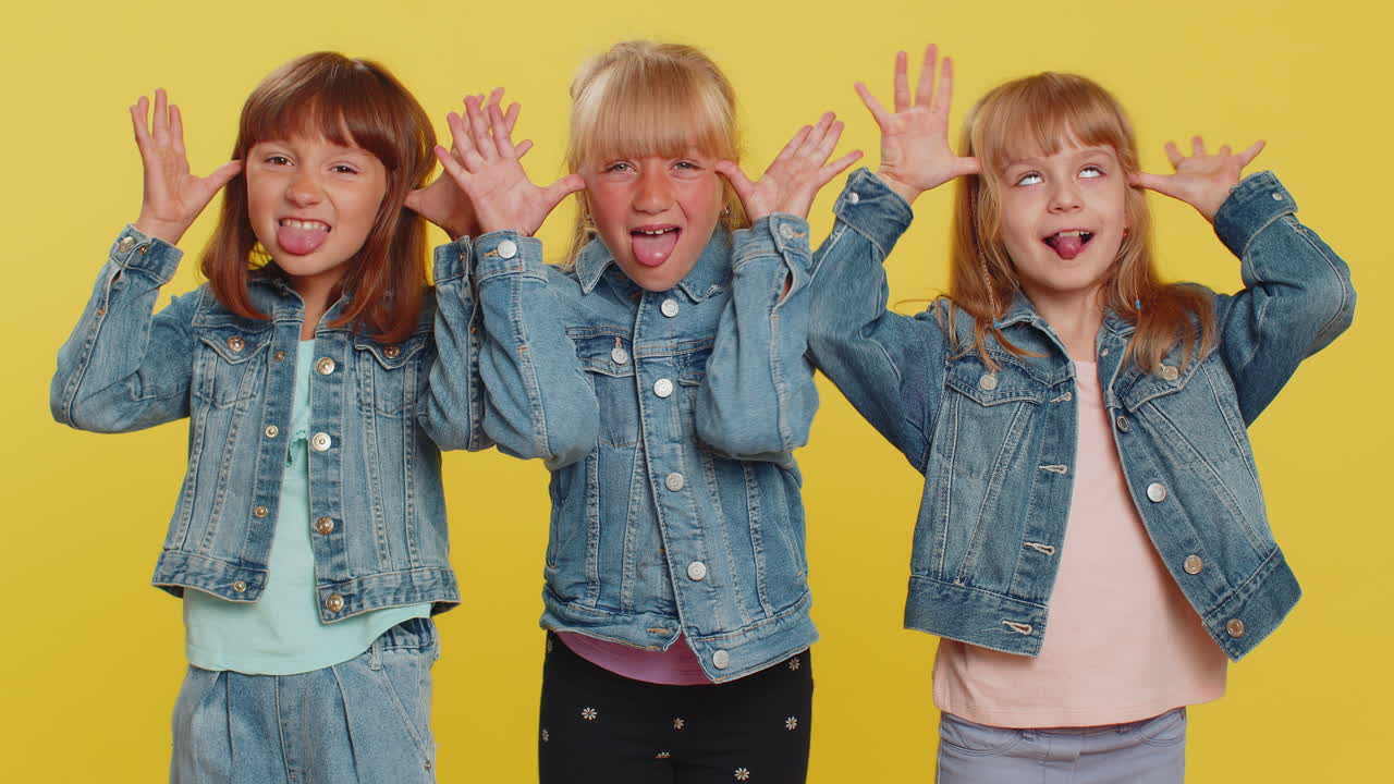 Three girls siblings friends showing tongue making silly faces fooling around joking teasing