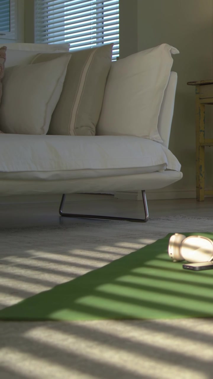 Vertical video: Panning camera revealing white sofa in living room, showing workout setup with mat