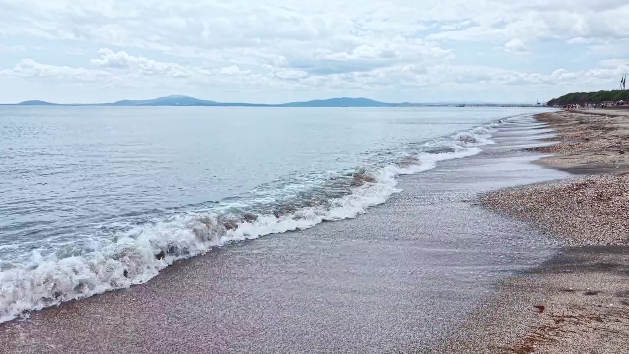 Calm waves wash onto the shore while clouds gather over the water during mid-afternoon in a quiet beach location