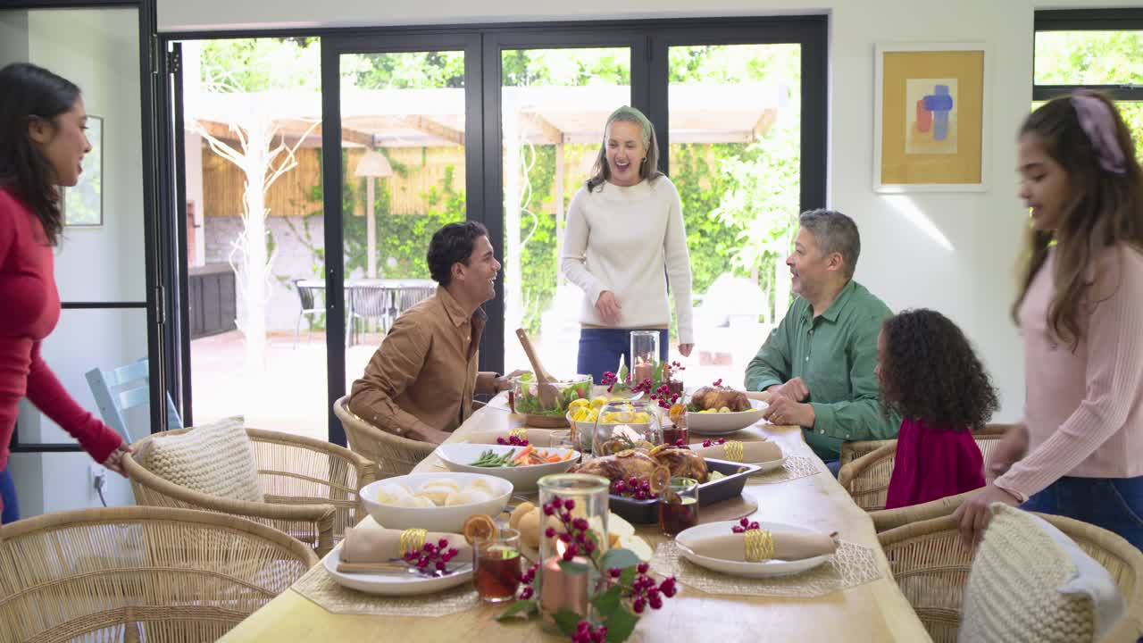 Diverse family carrying dishes toward wooden table at home for dinner, greeting and settling in