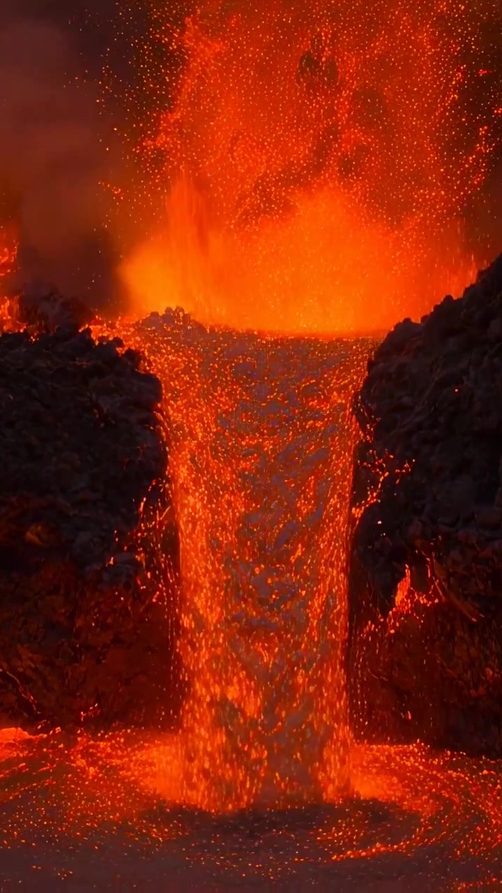 Vertical video: Pressure forcing lava fountain and narrow cascade flowing down vent into hot pool