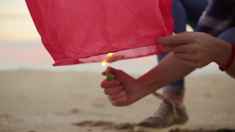 close up view of hands lightning before launching red paper lantern. female hands holding lantern with fire before to let it fly