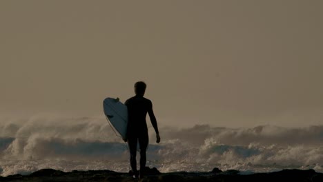 Silhouette of a surfer and waves at dusk
