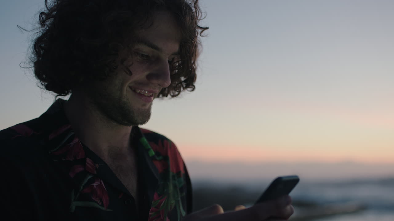 giovane uomo che usa il telefono per mandare messaggi sul mare in attesa del tramonto dell'alba