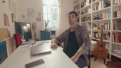 young man posing on camera at desk with laptop at home