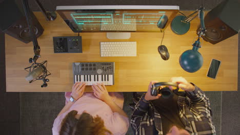 overhead view of male and female musicians at computer with keyboard in studio at night