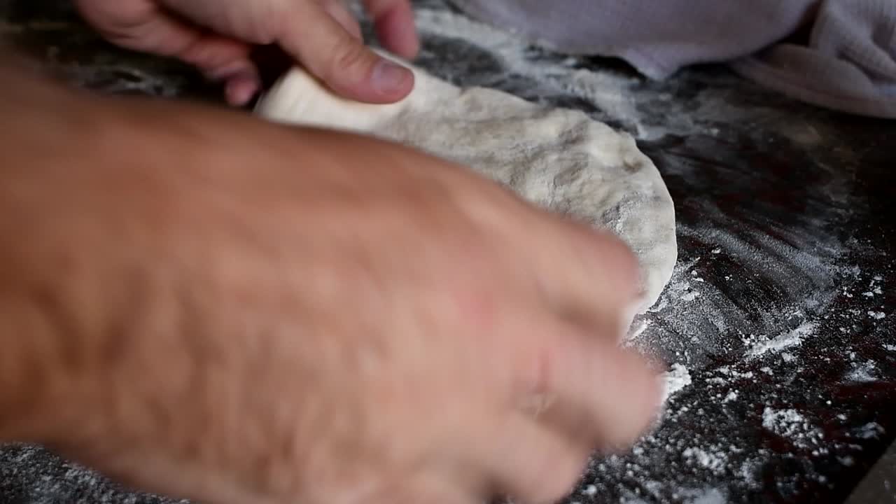 Working on a home made pizza dough with the bare hands on a marble kitchen counter. Side view, medium high angle. Natural window light