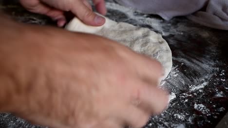 working on a home made pizza dough with the bare hands on a marble kitchen counter. side view, medium high angle. natural window light