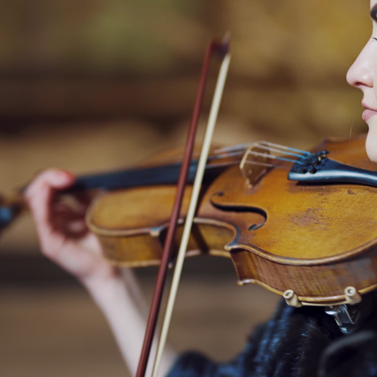 An attractive girl with long hair holds a violin in her hands and plays amazing melody on the background of high architecture in the city in the evening. Blurred background. Close-up