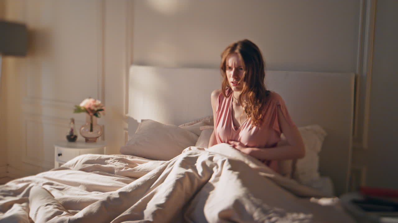 걱정스러운 여성은 아침에 배통을 고 있습니다. 깨어있는 슬픈 소녀는 배를 만니다.