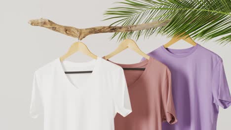 video of close up of white, beige and purple t shirts hanging on branch on white background