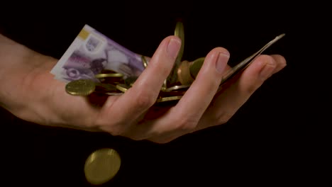 Pile-of-coins-money-falling-into-a-hand-of-cash-against-a-black-background-in-slow-motion