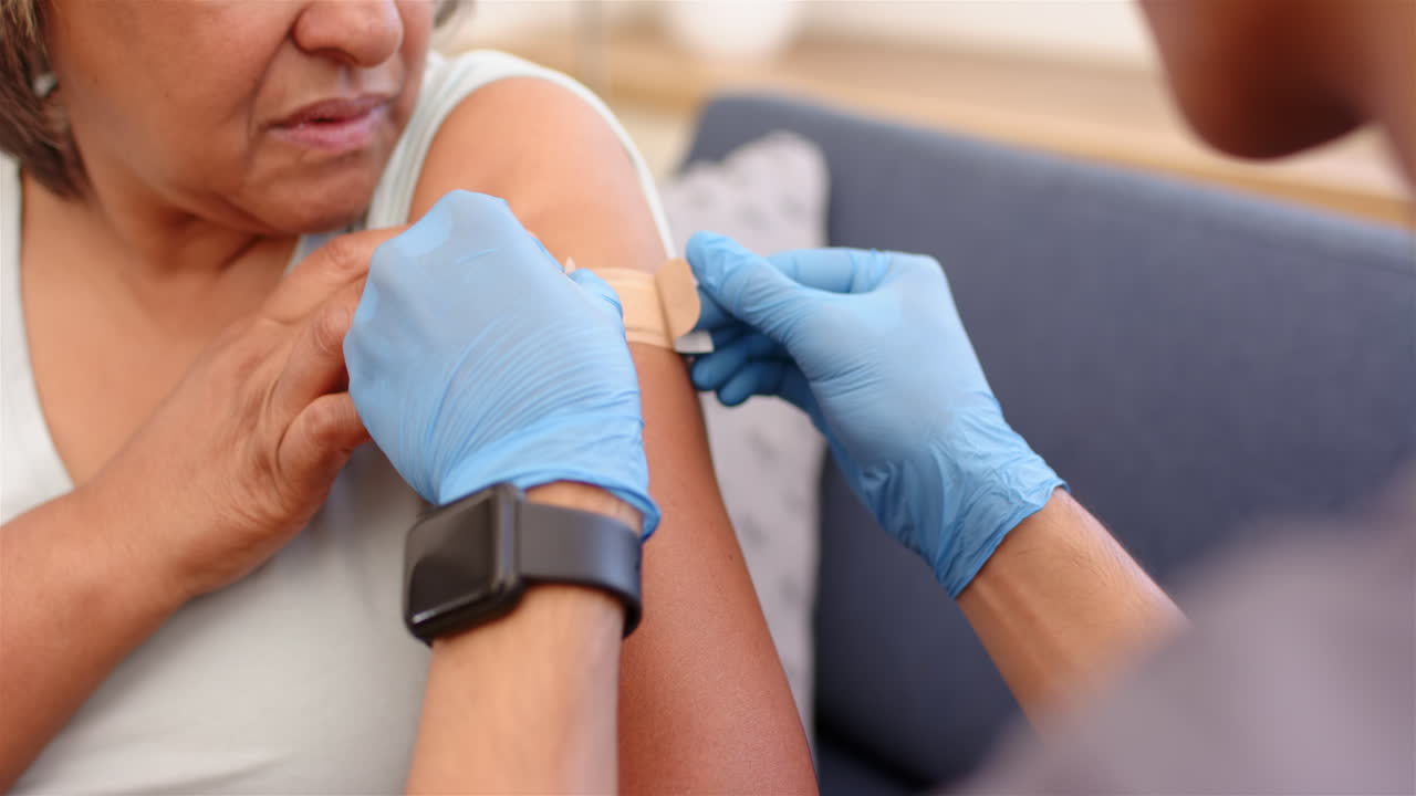Applying bandage, healthcare worker assists senior woman after school vaccination