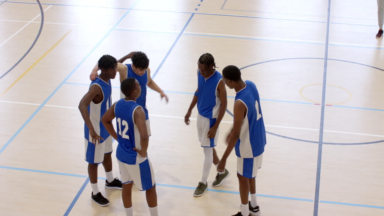 Multiracial male basketball players huddling with coach walking and observing game in gym