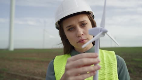 female caucasian engineer standing outdoors and checking wind turbine field plastic model.