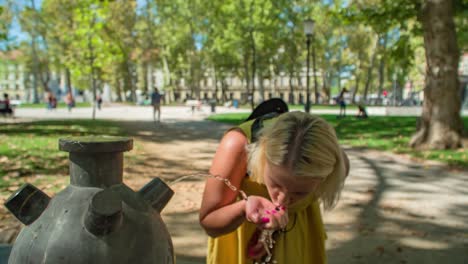 Nahaufnahme-Einer-Jungen-Frau-In-Gelbem-Kleid,-Die-Aus-Einem-öffentlichen-Wasserbrunnen-Trinkt