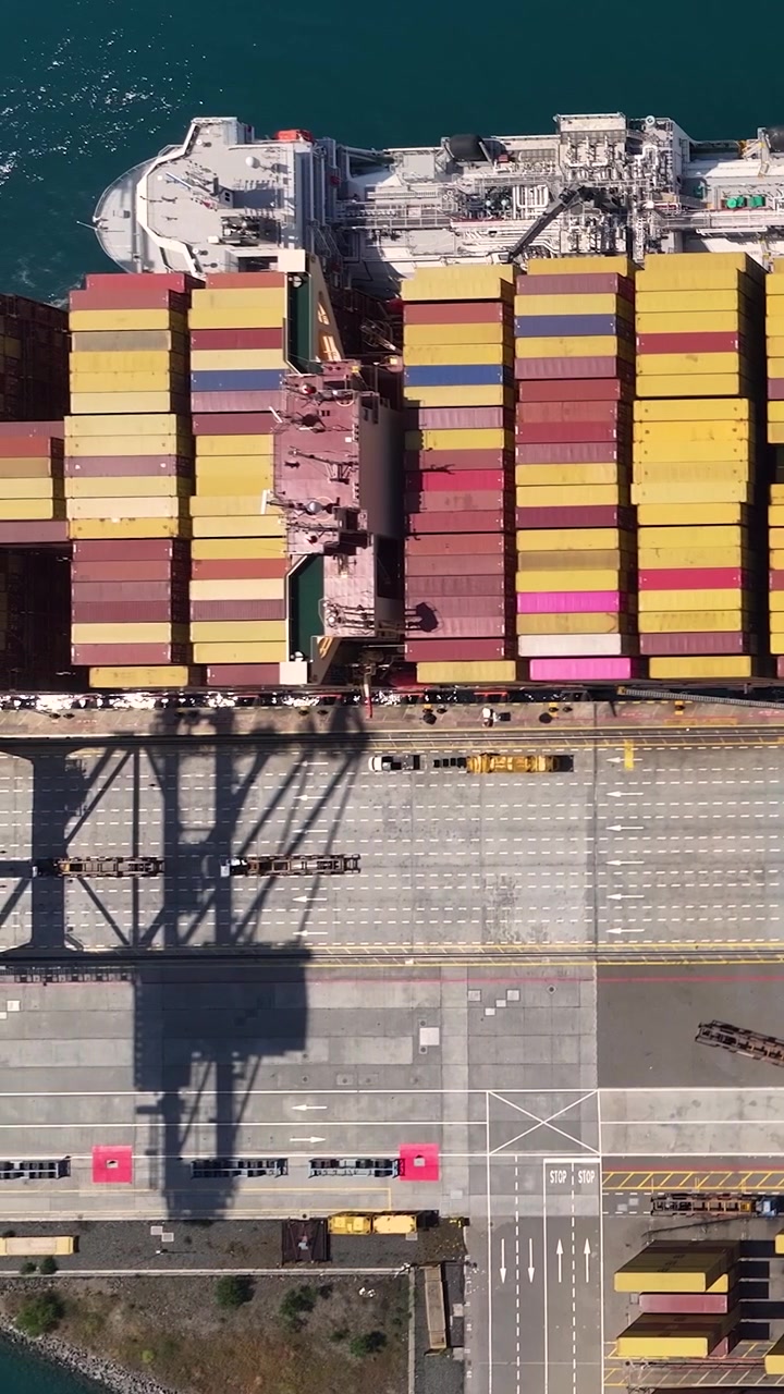 Una terminal de contenedores con un gran buque portacontenedores siendo cargado y descargado. Los contenedores de envío están organizados en filas a lo largo del muelle
