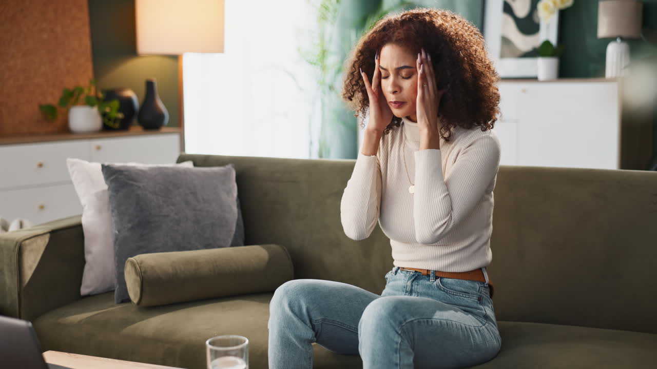 A woman takes medication with a glass of water on her couch