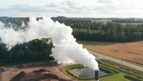 aerial drone shot of a lone factory chimney spewing fumes into atmosphere in rural area