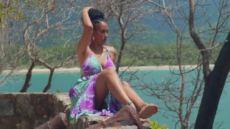 a woman in a graceful, long dress stands on a cliff, overlooking the serene beach below