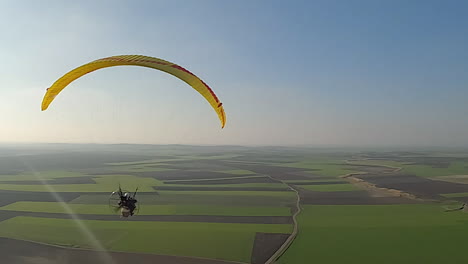 aerial follows paramotor in blue sky, propeller spinning below canopy