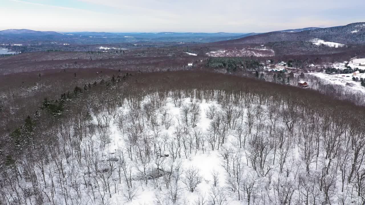 órbita aérea alrededor de la cima de una colina cubierta de nieve para revelar un lago azul entre un interminable bosque de invierno