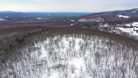 aerial orbit around the top of a snow covered hill to reveal a blue lake among an endless winter forest