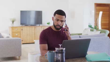 Mann-Spricht-Auf-Smartphone,-Während-Er-Zu-Hause-Einen-Laptop-Benutzt