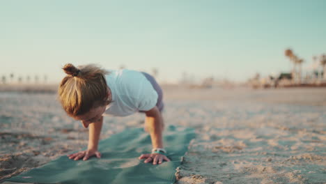 blonde woman exercising yoga on mat by the sea.