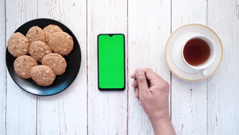 smartphone with green screen, cookies, and tea on a wooden table