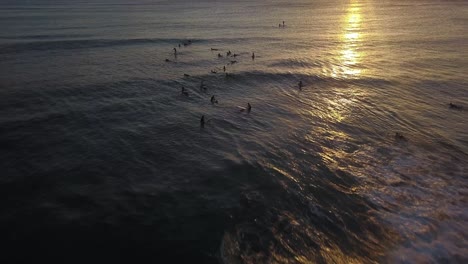 silhouette of surfers catching waves in golden sunset aerial tilt down