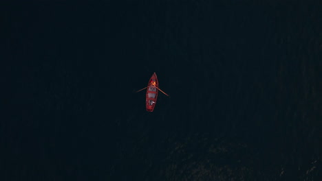 top down view of a red paddling boat in a deep dark blue lake