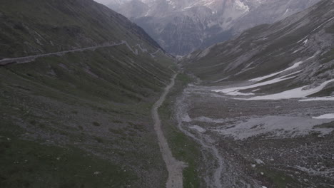 Drone-shot-flying-over-the-Stelvio-Pass-Italy-on-a-grey-day-going-to-the-scenic-view-of-the-snowy-mountains-in-the-background-on-a-grey-day-during-sunset-time-LOG